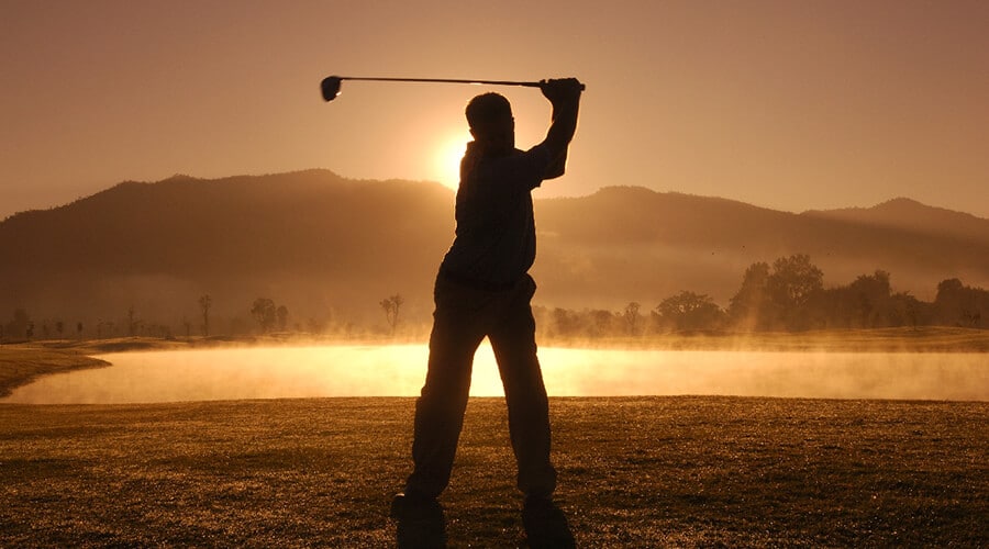 A golfer in silhouette against a sunset swinging a golf club